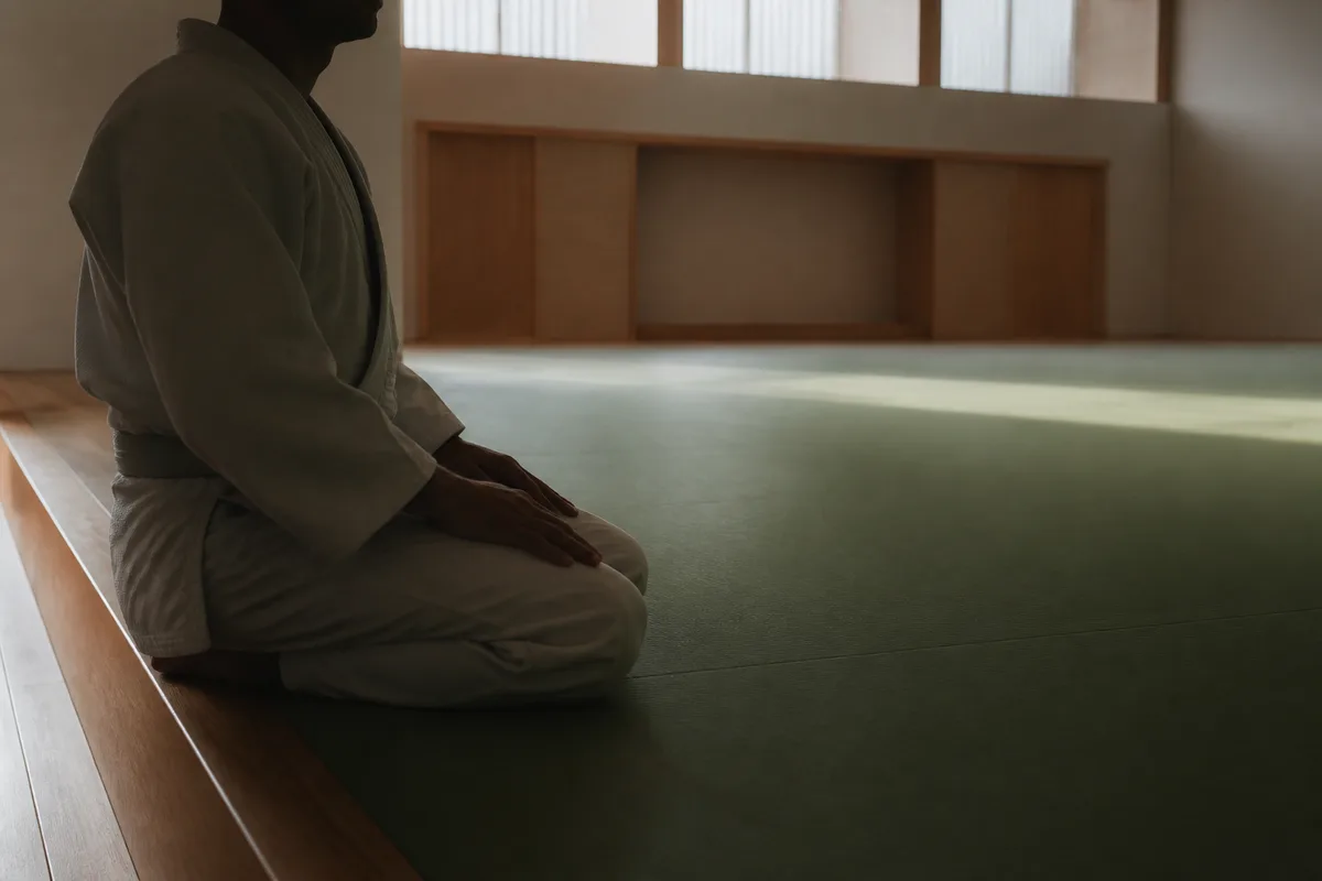 Judoka assis au bord d’un tatami, mains sur les genoux, respiration lente en fin de séance