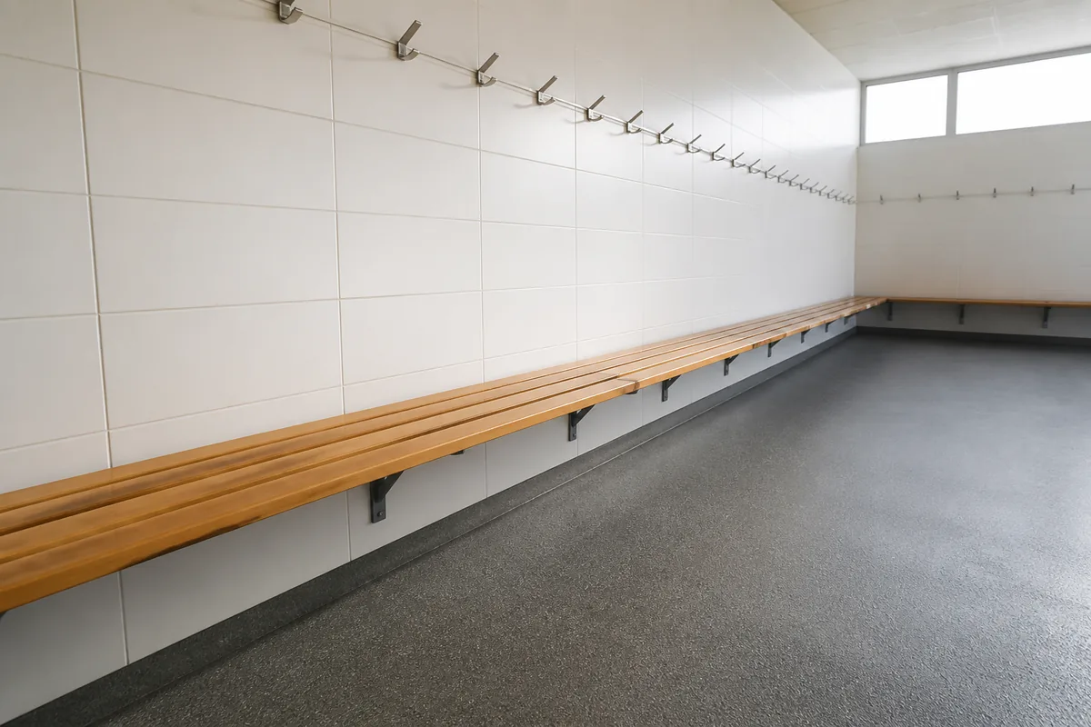 Vestiaire de club sportif avec bancs en bois clair et patères métalliques, lumière naturelle latérale