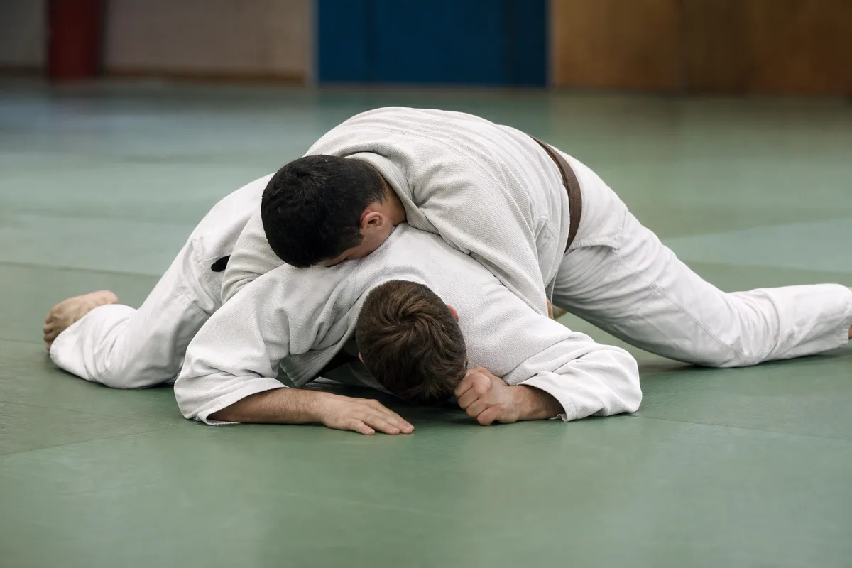 Deux judokas en kimono blanc travaillant une immobilisation au sol sur un tatami vert de dojo