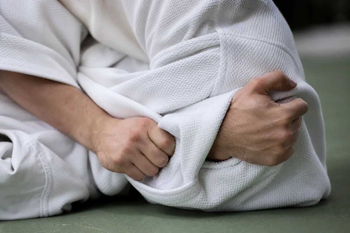 Judoka appliquant un contrôle latéral en kesa-gatame, mains en gros plan sur le judogi blanc