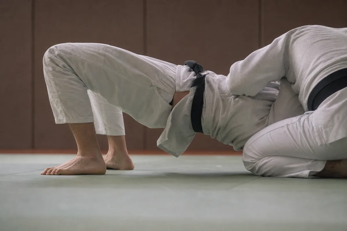 Judoka en position de pont au sol cherchant à se dégager d&rsquo;une immobilisation, vue latérale sur tatami