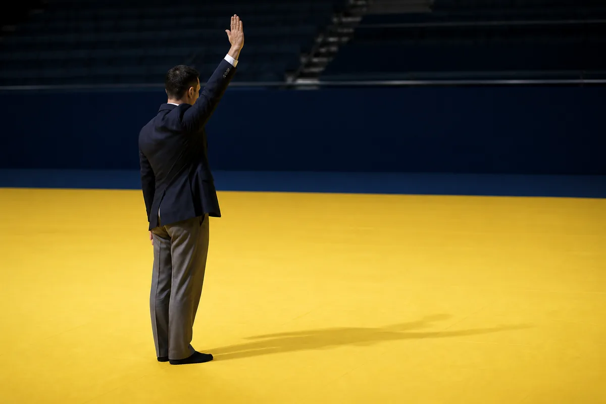 Deux judokas en judogi blanc au moment d’une projection, l’un en suspension au-dessus de la hanche de l’autre sur un tatami vert