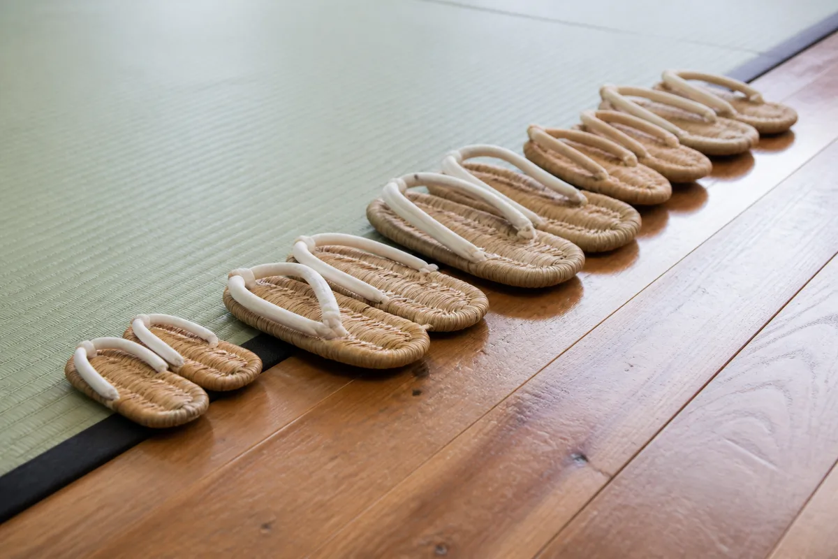 Rangée de zoris alignés au bord d’un tatami de dojo