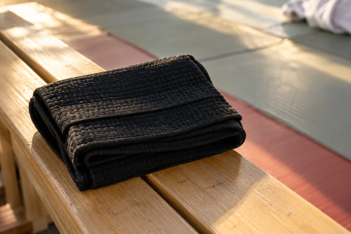 Ceinture de judo pliée posée sur un banc de dojo en bois