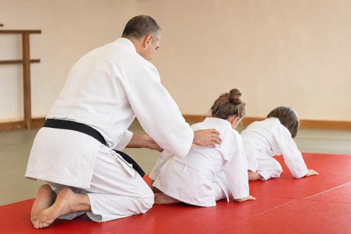 Enseignant de judo en ceinture noire guidant de jeunes pratiquants lors d’un cours sur le tatami