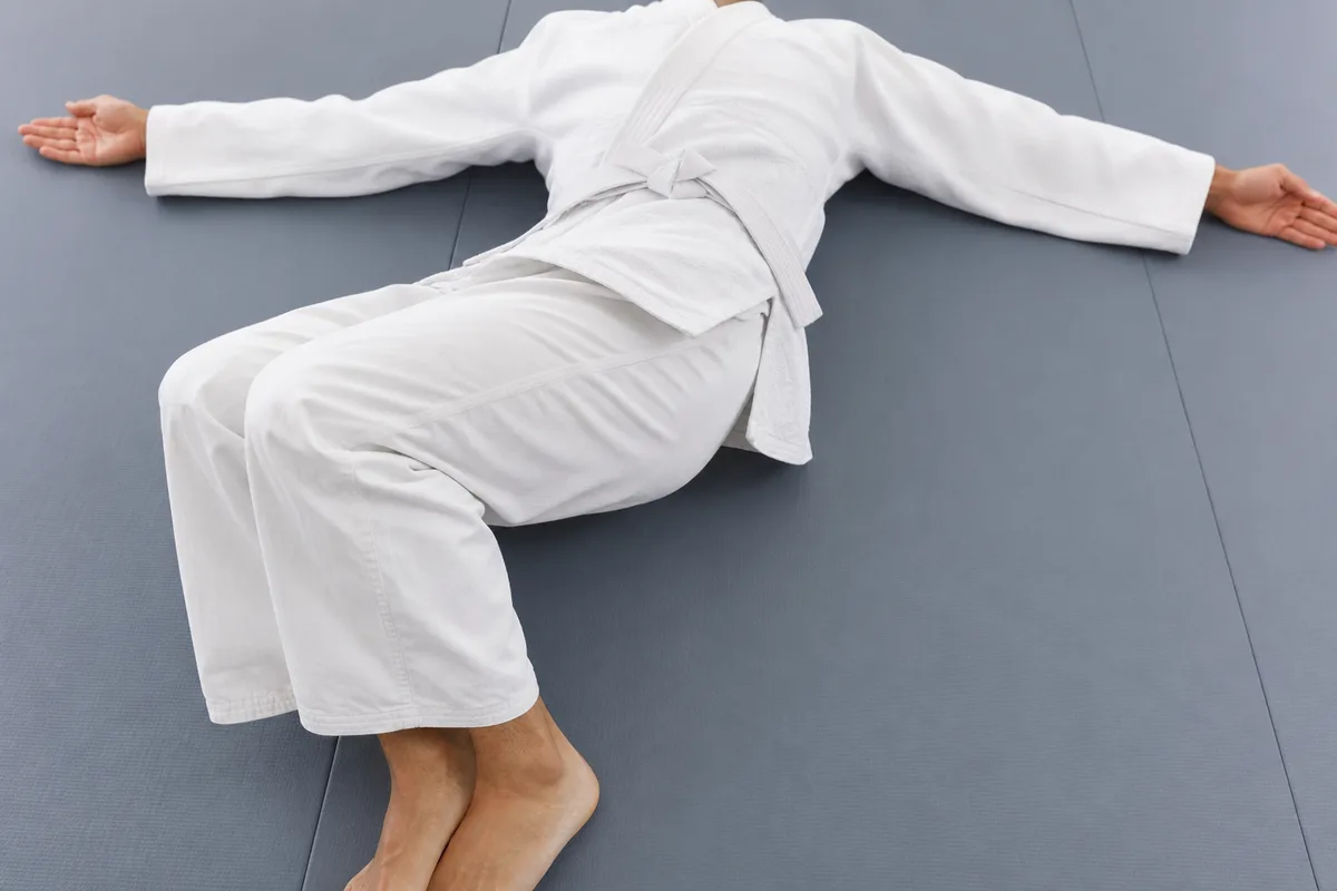 Ouverture thoracique au sol, bras en croix, sur un tatami de dojo