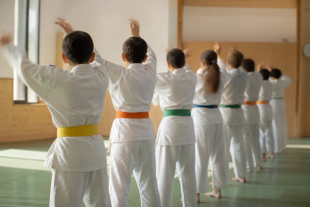 Judokas en judogi blanc alignés de dos en début de séance sur un tatami vert