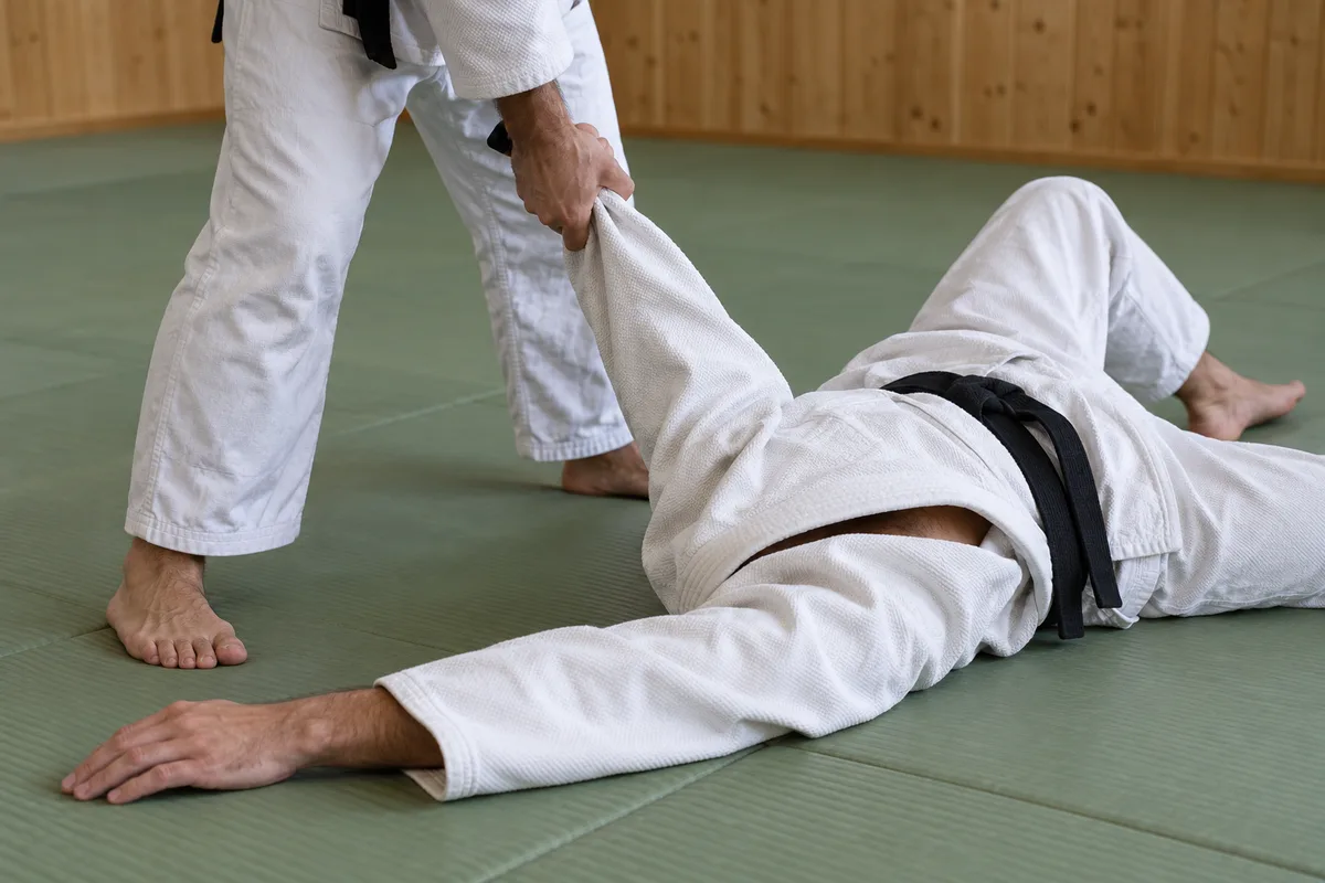 Partenaire debout gardant la manche d’un judoka qui termine sa chute sur le dos au tatami