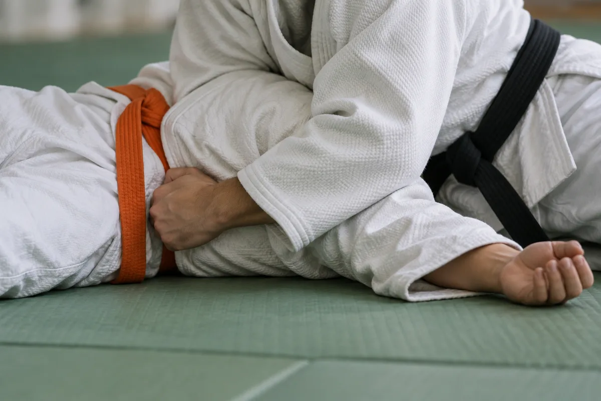 Deux judokas au sol en immobilisation, cadrage sur les judogis et les ceintures, visages hors champ